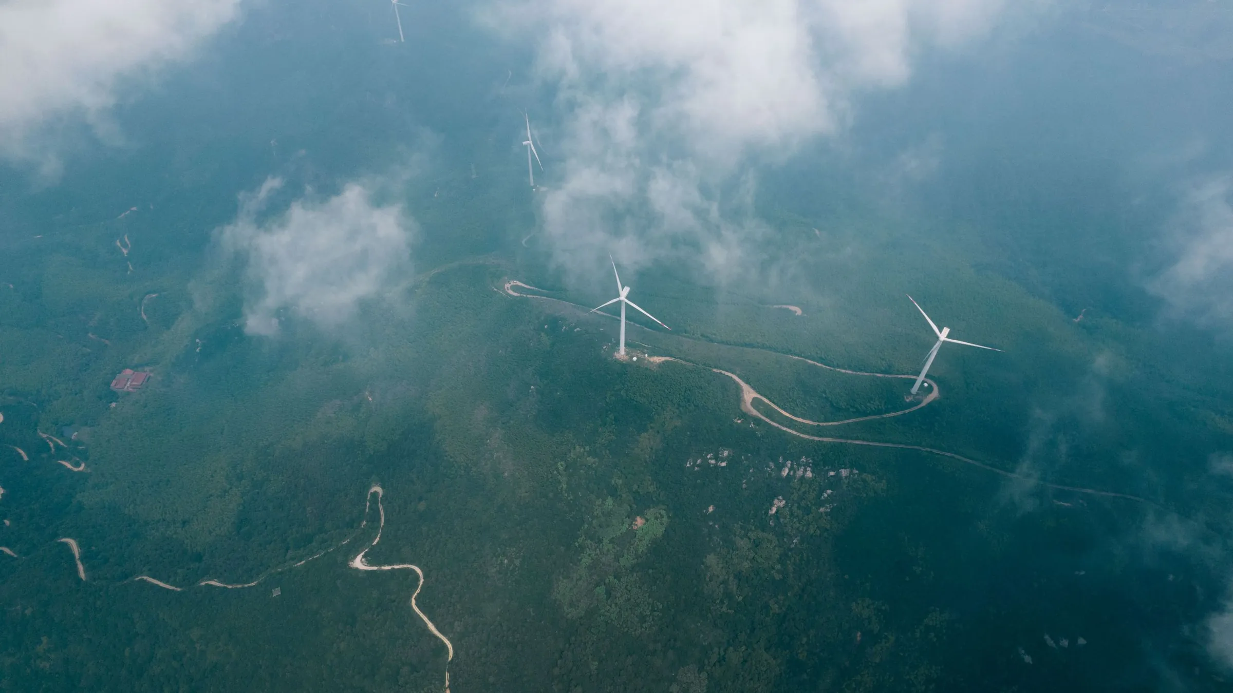 Low cloud drifting over wind turbines on green hills, seen from above